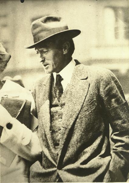 Candid shot of the writer, perhaps Upton Sinclair or Clement Wood, wearing a hat and a tweed suit.