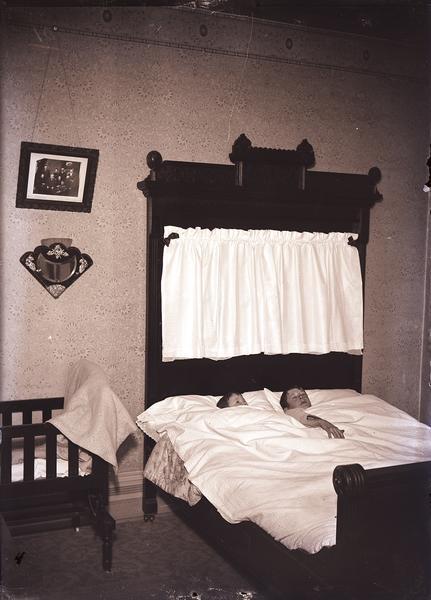 Bedroom scene with two boys in a bed with ornate headboard.