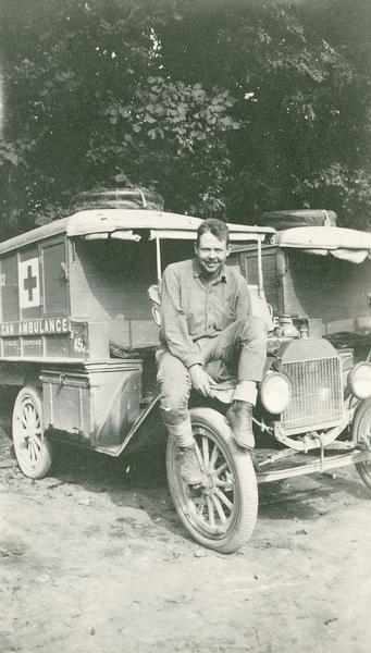 An ambulance man (presumably Ray E. Williams) sitting on the front fender of an American ambulance.