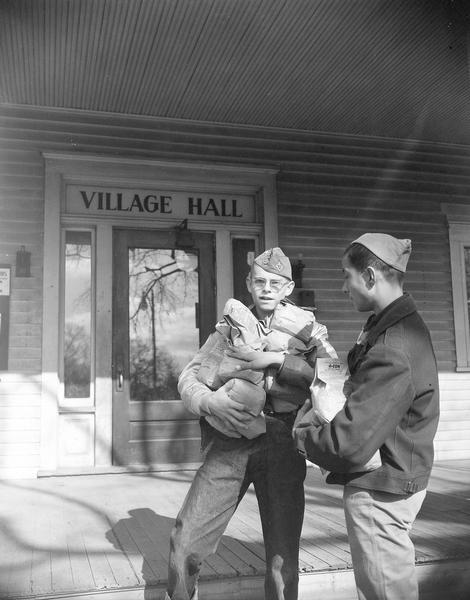 A man distributes rat poison, which was invented by Dr. Link, to a Boy Scout to place in rat-infested areas. They are standing in front of the Village Hall.
