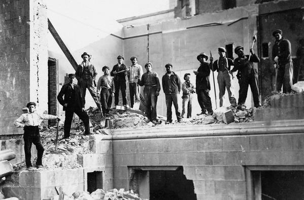 Workmen demolishing the North Wing of the third Wisconsin State Capitol. Because the North Wing escaped damage during the fire in 1904, the North Wing continued to be used for several years.  The workers' presence in this photograph serves as a gauge by which to measure the size of the Prairie du Chien sandstone blocks from which the third Capitol was constructed.