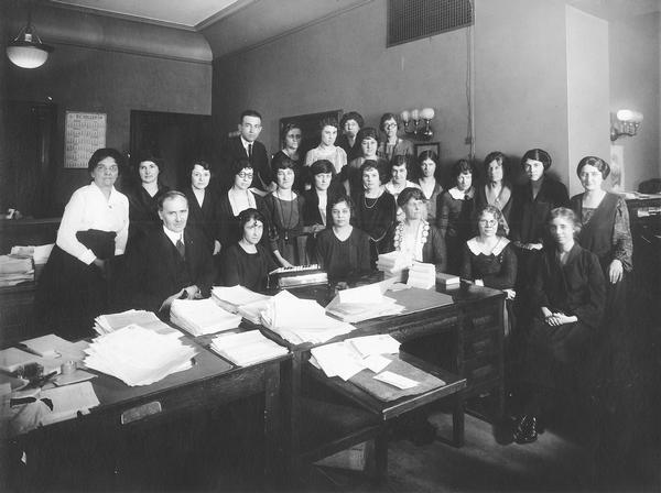 Group portrait of the Industrial Commission staff. Back row: A.J. Altmeyer, Elva Norris, Isabelle Kriuse, Clara Brigg, Lillian Rhoder, Marian Hall. Middle row: Miss Wisster, Blanche Miller, Marie Cambir, Esther Vluingerhaquist Brakary, Genivieve Lobiman, Leva Purcall, Helen Gill, Stella Rolfman, Katherine Dagney, Adella Stords, Marie Endies, Clarabeth Viji. Seated: I.M. Wilcox, Ronille Brennan, Arlene Sehrasder, Kettie Blord, Gladys Wagner, Grace Gomey. At the time this was taken, Altmeyer was Chief Statistician of the Commission in 1920 and later became its Executive Secretary in 1922.
