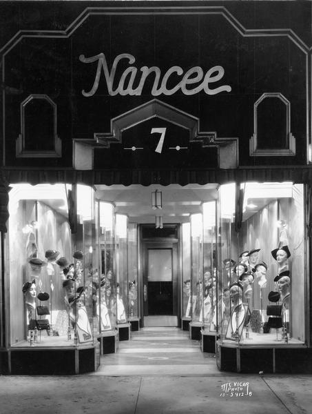 Exterior night view of the Nancee Hat Shop at 7 South Pinckney Street featuring hats, purses and an Art Deco entrance.
