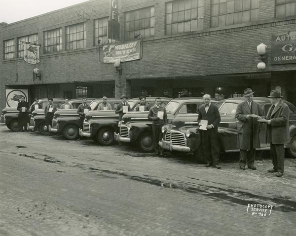 Six Chevrolet automobiles (possibly taxies) and 10 drivers holding pledge cards outside the side entrance to Friede Storage Garage (previously known as Purcell's Auto Co.), 434 W. Gilman Street. One of the men is handing pledge card to another man. This could be City Car Company taxis and drivers.