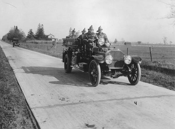 Four men dressed in fire fighting gear driving a fire truck on State Highway 47 near Appleton.  The Wisconsin Highway Commission which published this photograph in its 1918 annual report wrote "good roads will make adequate rural fire protection possible."