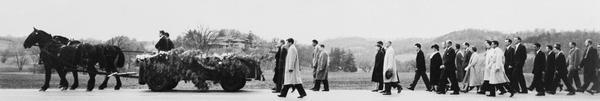 Panoramic view of the funeral procession of architect Frank Lloyd Wright, with Taliesin seen in the center background. Following the farm wagon hearse are Wright's wife and his daughter Iovanna, as well as former students and members of the Wright Fellowship. Taliesin is located in the vicinity of Spring Green, Wisconsin.