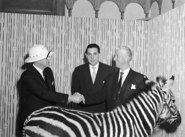 Marlin Perkins shaking hands behind a zebra.