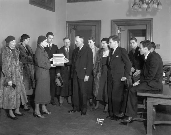 University of Wisconsin students representing the U.W. Student Budget Committee present a petition to Senator Otto Mueller at the Wisconsin State Capitol. Stella Whitefield, President of the Women's Self-Government Association hands petitions that object to university budget cuts to the senator. Other students are Jean Teitkamp, Virginia Vollmer, Arthur Lueck, John Butterwick, Martha Adams, Nora Kahn, Herman Sommers, Ted Wadsworth and Kenneth Meiklejohn.
