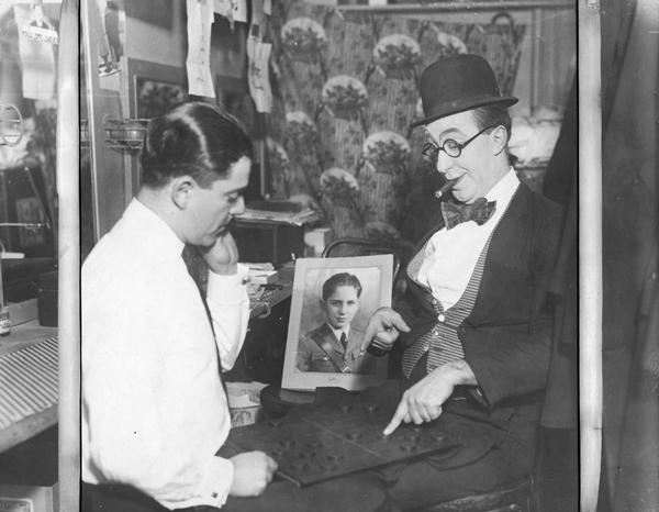 Ed Wynn, in makeup for "Manhattan Mary," plays checkers with George White.