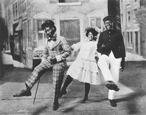 George Walker, Adah Overton Walker, and Bert Williams link arms and dance the cakewalk in the first Broadway musical to be written and performed by African Americans, <i>In Dahomey</i>.