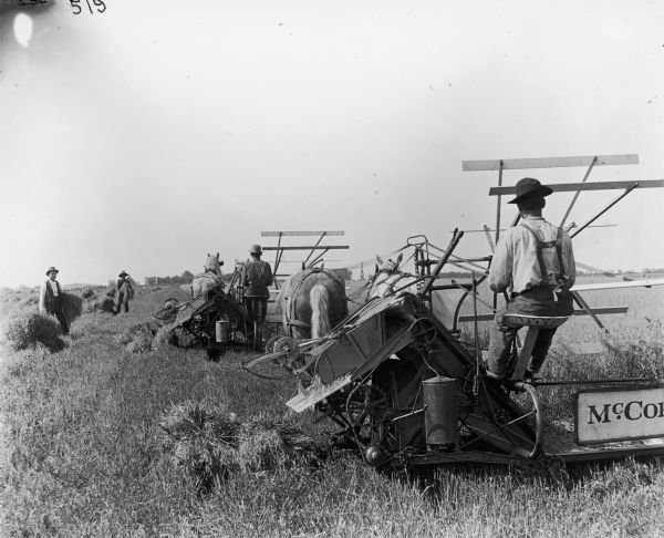 Four men harvesting grain in a field with two horse-drawn McCormick binders. (D.R. Robbins?) 