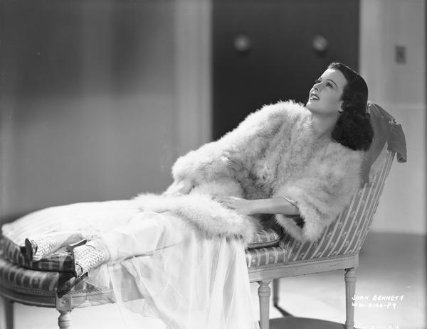 Publicity shot of Joan Bennett for "The House Across The Bay" showing her in furs reclining on a chaise.