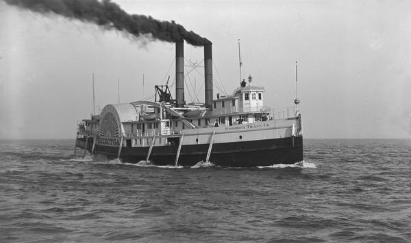 View across water towards the Sheboygan Lake steamboat out on the water, with several passengers visible on the deck.