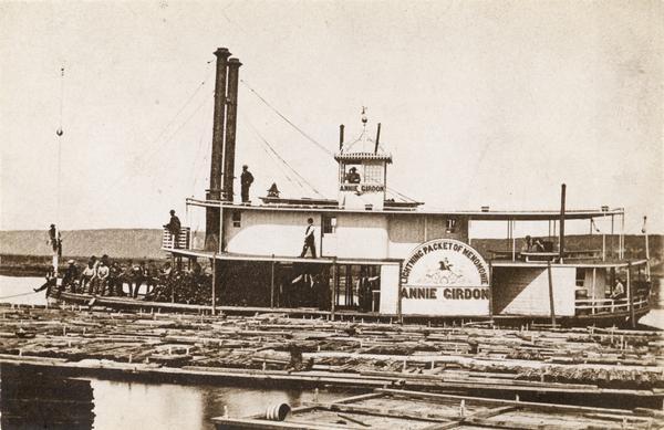 Sidewheel rafter, <i>Annie Girdon</i>. The crew is on deck and a raft of logs is in the foreground. Sign on wheel reads <i>Annie Girdon</i>, lightning packet of Menomonie. Capt. Dan Davison is on the upper deck near stacks. Pilot William Wooden in the Pilot House. Clerk Chas N. Edwards forward by crate that held check lines. Harvey Black and wife, cooks, on stern. The Indian on horseback "going like the wind," with drawn bow, was painted by G. Ordemann of Menomonie, Wisconsin. When the boat was repainted at Rock Island in the spring of 1871, the painter painted out the Indian and the words Lightning Packet of Menomonie-and could not reproduce them.