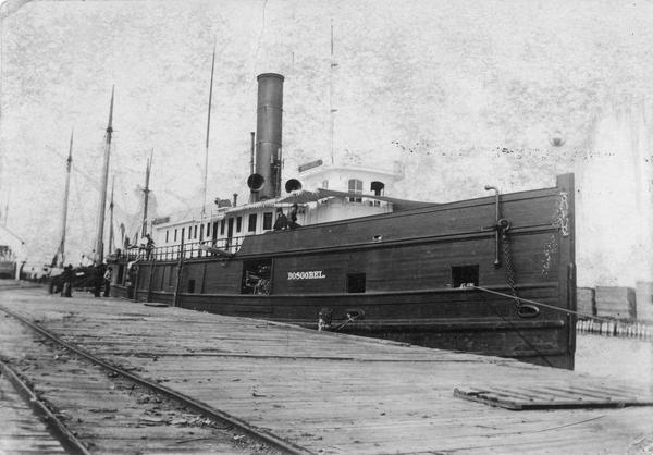 The screw tug, "Boscobel" built in 1881, is at a wooden dock with cordwood stacked on deck inside her forward gangway, perhaps indicating that she burned wood for fuel. Later named the "Ottawa."