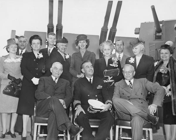 The official delegation party with their wives at the ceremony of silver service presentation aboard the USS "Wisconsin". Seated left to right are Judge Rosenberry, Captain Roper, and Lieutenant Governor Oscar Rennebohm. Standing left to right are Mrs. Scwanke, Mrs. Doan, Mrs. Rosenberry, Miss Mary Hope Martin, Mrs. Roper, John E. Dickinson, Mrs. Rennebohm, and Mrs. Dickinson.