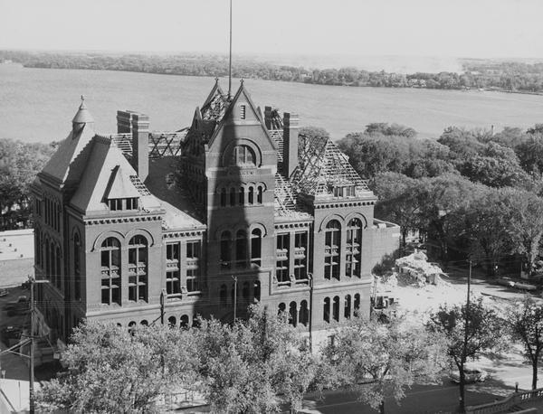 Elevated view of the Dane County Courthouse as it is being razed. Much of it is still intact in this image. Lake Monona and Monona Bay are in the distance.