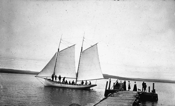Sailboat <i>Lizzie W.</i> at the Mission Dock. Captain Daniel Russell Angus, in the white sleeves, is at the tiller. The boat was named after Elizabeth Woods, the wife of Frederick Woods.