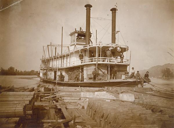 The sternwheel rafter, "Juniata," pushing a raft of lumber. The crew is posing on deck. The boat was later named "Red Wing."