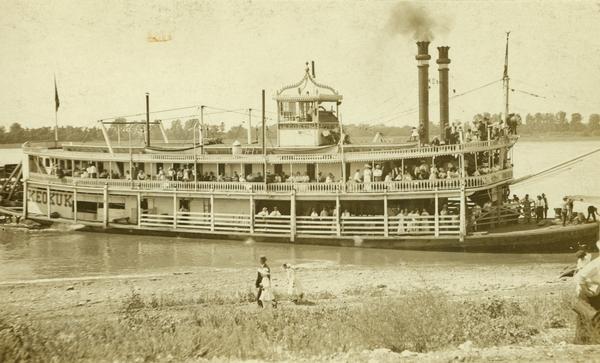 The sternwheel packet, "Keokuk," at a landing during August, 1913. Several people watch from shore. The "Keokuk" operated between Keokuk and Quincy, Illinois.