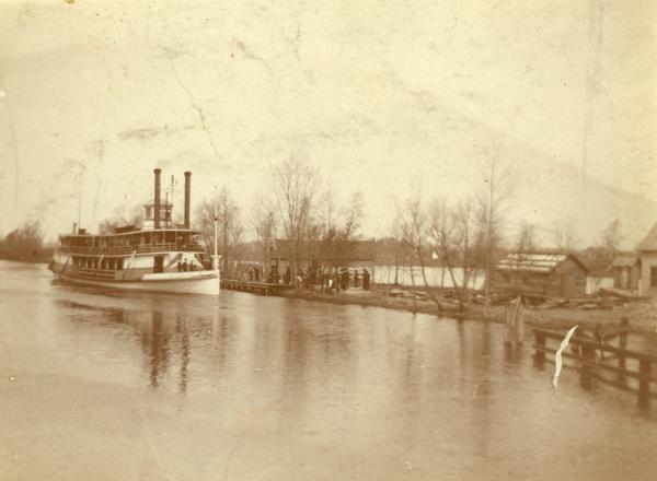The sternwheel excursion, Thistle, by a landing. Passengers wait on shore. Previously named J.H. Crawford. The Thistle ran between Oshkosh and Omro, WI via Lake Butte des Morts.
