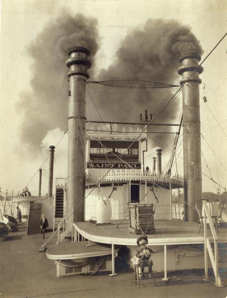 The upper deck of the sidewheel excursion, "Saint Paul" with smoke streaming from smokestacks. A child is sitting in a chair on the deck. Later named Senator.