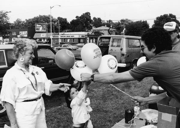 A man gives a little girl balloons that say "Jobs With Justice".