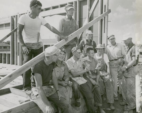 A group of carpenters pose in front of an unfinished building. The caption reads "Carpenters union donate wages to community fund".