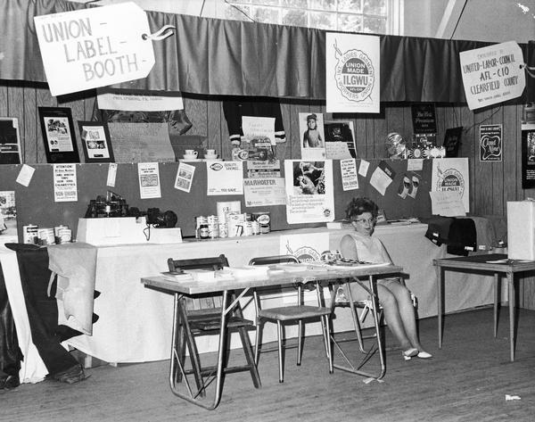 A woman sits at a Union Label booth, perhaps at a county or state fair.