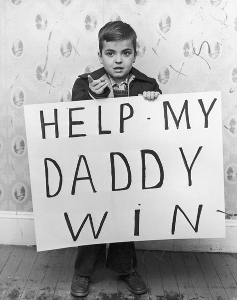 Kensell Willingham, son of a worker out for eight months on strike against O'Sullivan Rubber Company, holds a sign that reads "Help My Daddy Win". Caption taped on the back of the original reads: "The Winchester, Virginia Corporation is now trying to break his daddy's union by importing out-of-state strikebreakers. You can help Kensell's daddy win the strike by refusing to buy O'Sullivan heels and soles. Show how you feel. Don't buy from America's No. 1 Heel."