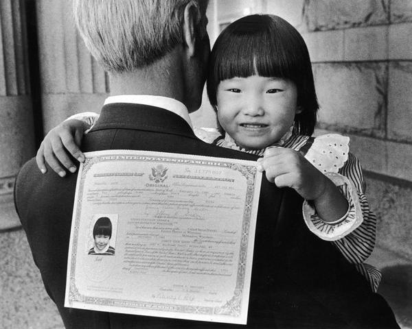 Jennie Youn Haeng Seider, 4, of Milwaukee, used her father Jeffrey Seider's back to display her new certificate of naturalization.