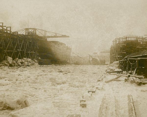 The American Shipbuilding Company yard in winter with ships and a derrick in the center of the image.