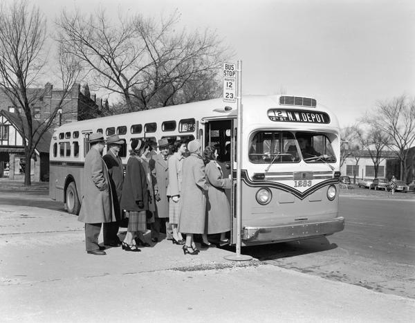 A group of people boarding a diesel bus on 12th Street.