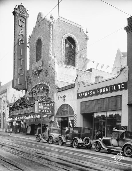 View from across the street of the Capitol Theatre tower. "Love Parade" is advertised on the marquee. Three automobiles are in the street in front of Peoples Clothing Store at 213 State Street, and Farness Furniture store at 215 State Street.