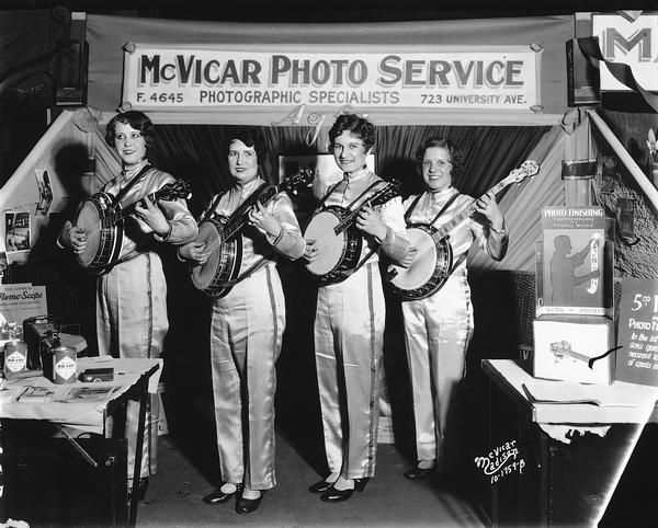 Four women are playing banjos in the McVicar Photo Service Booth at the 1930 East Side Businessman's Association (ESBMA) Fall Festival.