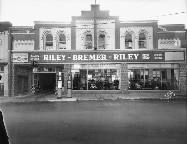 The Riley-Bremer-Riley Oldsmobile garage on E. Doty Street began as the Riley Livery Stable when horse-drawn transportation reigned and then transitioned to automobiles. There are gas pumps at the curbside.
