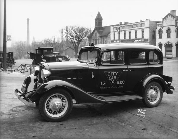 A new Chevrolet City Car Company cab owned by James and Grace Riddell. In the background is a view of the 200 block of East Washington Avenue. 