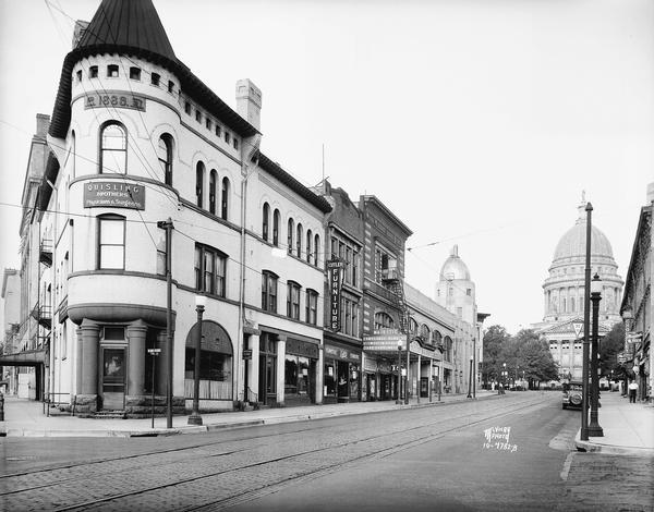 Office of the Wisconsin State Employment Service. View of King Street looking toward Capitol Square from East Doty Street. Businesses in view include Quisling Clinic (in this building 1933-1946)at 123 King Street, Pickard Furs at 121 King Street, Cutler Furniture at 119 King Street, Majestic Theater at 115-117 King Street, Madison Liquor store at 113 King Street, Capitol City Bank at 111 King Street, Arcade Barbershop at 109 King Street, Charlier and Son Jewelry Company at 107 King Street. The Wisconsin State Capitol is in the background.