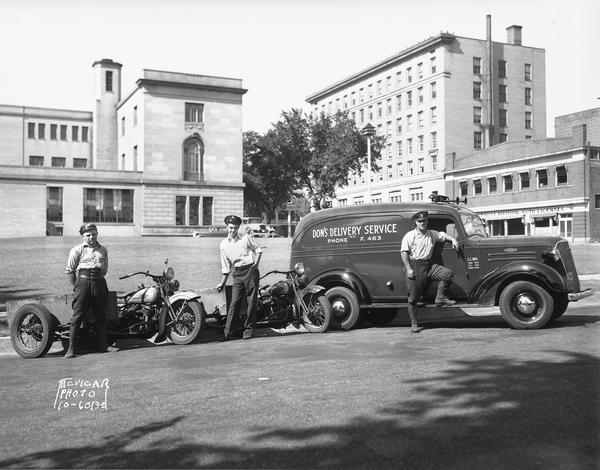 Employees of Don's Delivery Service, Inc. near the main Post Office, with Harley Davidson motorcycles and a closed panel truck. They are parked across the street from their office at 209 S. Pinckney Street, with the National Mutual Insurance (Beaver building), 119-23 Monona Avenue, the Wisconsin Automobile License Division, 16-20 Doty Street, and the rear of the U.S. Post Office, 215 Monona Avenue, in the background.