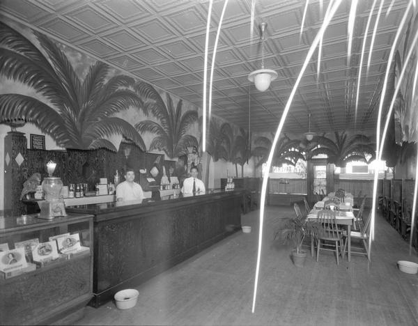 Interior of Urso's West Side Palm Tavern with two bartenders, cigar display, tin ceiling and palms. The tavern was located at 734 West Washington Avenue in the Greenbush neighborhood.