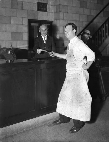Charles Palmeri, aka Pasquale, in an apron, receives a check from James Lewis, Special Deputy representing the street banking commission, to settle his account at the bankrupt Capital City Bank. Palmeri owned a shoe shop at 110 South Pinckney.