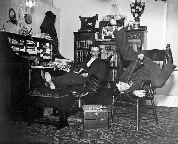 A medical student is playing with electric shock equipment as Dr. Eugene Krohn, sitting at his desk with his feet up, is looking on. This is a carefully posed photograph of uncertain but probably humorous meaning.