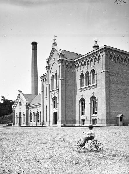 Exterior view of the Milwaukee Water Works. A little boy is riding a tricycle in the foreground.