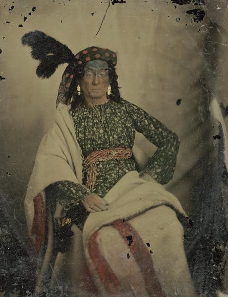 A woman dressed in Indian headwrap with feather, wrapped in a blanket, for a performance of "Black Hawk, or Lily of the Prairie," written by Mary Elizabeth Mears of Fond du Lac, Wisconsin, and presented in Madison, Wisconsin in 1857. Hand-colored ambrotype.