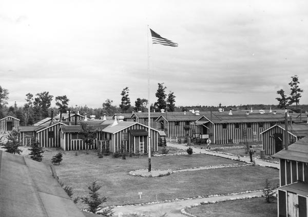 View overlooking Long Lake C.C.C. Camp with exteriors of buildings and flagpole.