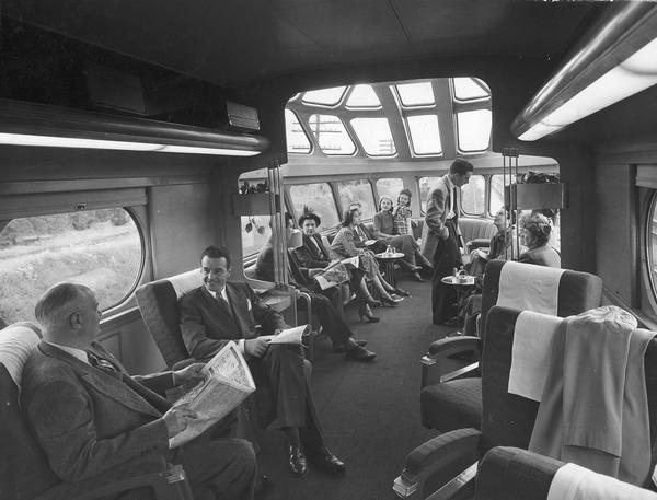 Interior view of people seated in the Hiawatha's observation parlor with sky-top solar lounge. The Hiawatha was signature high-speed passenger train for the Chicago, Milwaukee and St. Paul Railroad during the 1930s.