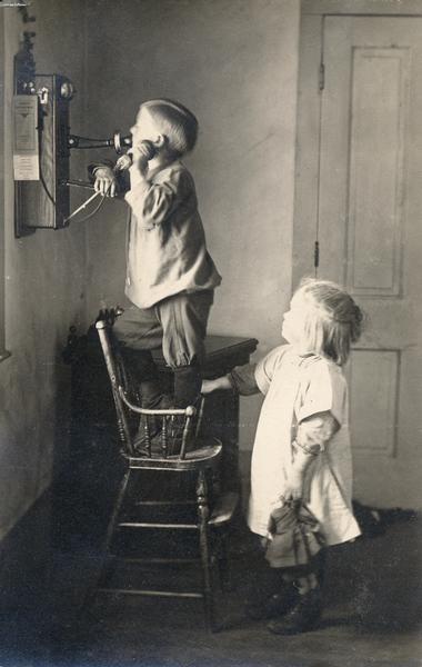 Laurie and Muriel Peterson, children of the photographer, use a high chair to talk on the phone.