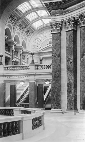 Interior of the east gallery of the Wisconsin State Capitol. By 1911, the commission learned that the quarry that supplied the red granite for the piers on the first floor of the Rotunda was nearly exhausted. At Post's urging the commission quickly procured enough of the red granite to complete the remaing piers and preserve the critical sense of geometry.