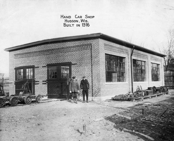 Two men stand in front of the Hand Car Shop, which was built in 1916.