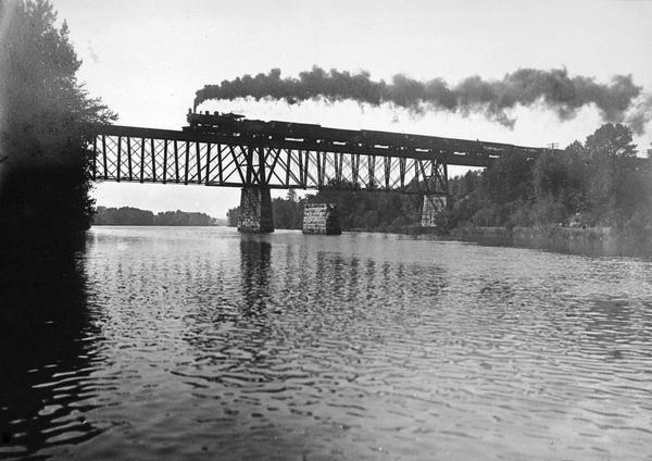 The railroad trestle over the Red Cedar River with a steam train passing over.